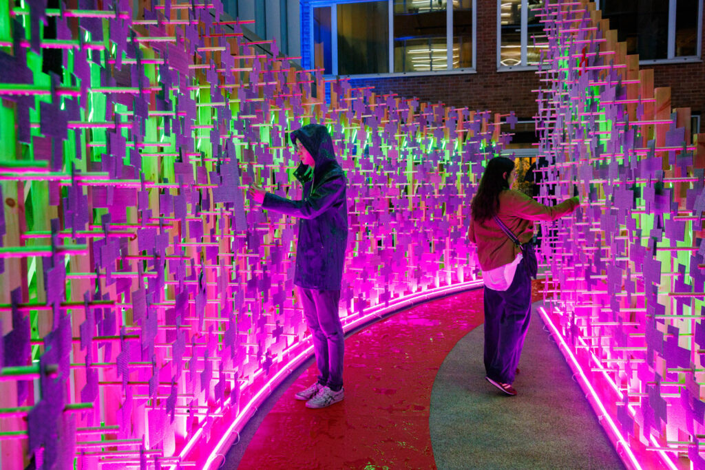 two people looking at a pink glowing wall installation