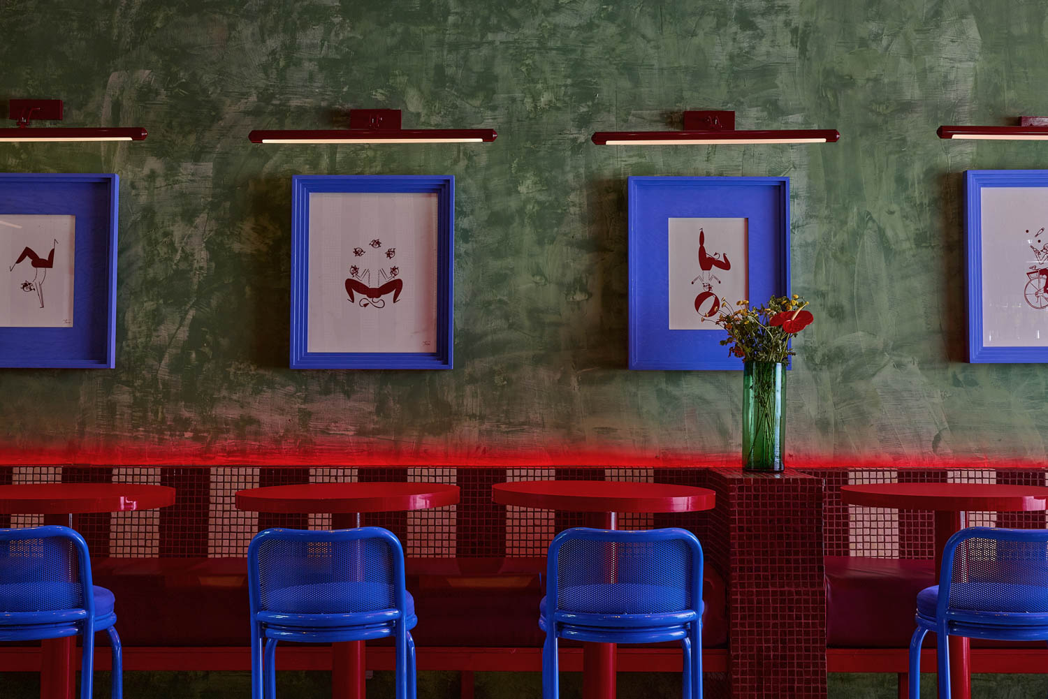 dining area with bright blue chairs, artwork and red tables by Maye Ruiz