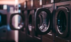 A dark room of a publiс laundry with a row of empty washing machines inside, selective focus on the opened door of one of the tumble dryers, shallow depth of field, strong bokeh in the background