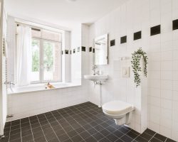 Flush toilet located between sink and shower in small tiled bathroom of contemporary apartment